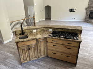 Kitchen featuring light wood finished floors, brown cabinetry, open floor plan, arched walkways, and black gas stovetop