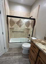 Bathroom featuring combined bath / shower with glass door, vanity, and light  finished floors