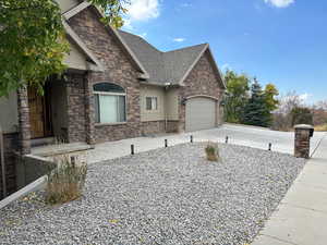 View of home's exterior featuring driveway, roof with shingles, a garage, and stone siding