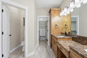 Primary bathroom featuring a walk in closet, double vanity, and light wood-type flooring
