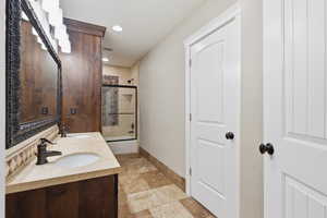 Main floor bathroom with combined bath / shower with glass door, double vanity, stone tile flooring, and recessed lighting