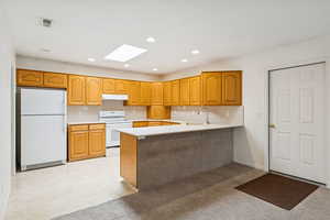 Kitchen featuring white appliances, light countertops, a peninsula, a skylight, and recessed lighting