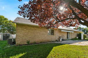 Back of house with a lawn, brick siding, a storage unit, and a shingled roof