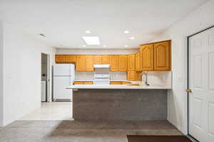 Kitchen featuring light countertops, white appliances, a peninsula, recessed lighting, and under cabinet range hood