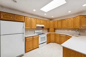 Kitchen featuring white appliances, brown cabinets, light floors, recessed lighting, and under cabinet range hood