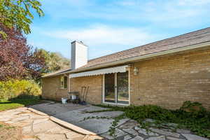 Rear view of house with a patio, a chimney, brick siding, and a shingled roof