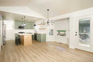 Kitchen with green cabinetry, a chandelier, open shelves, a breakfast bar area, and vaulted ceiling