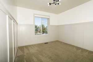 Empty room with a decorative wall, a wainscoted wall, carpet, and a chandelier