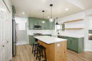 Kitchen with green cabinets, light wood-type flooring, appliances with stainless steel finishes, a breakfast bar, and tasteful backsplash