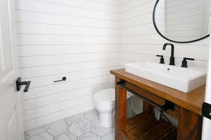 Half bathroom with marble finish flooring, vanity, and wooden walls