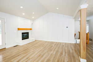 Unfurnished living room featuring vaulted ceiling, light wood finished floors, a brick fireplace, and recessed lighting