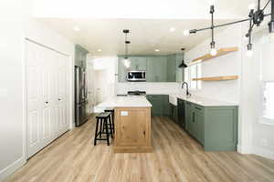 Kitchen featuring green cabinets, tasteful backsplash, a breakfast bar area, decorative light fixtures, and light wood-type flooring