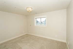 Carpeted empty room featuring baseboards and a chandelier