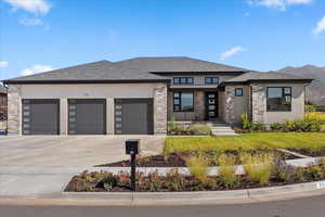 Prairie-style home with a shingled roof, concrete driveway, stucco siding, a garage, and a front lawn