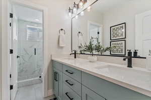 Bathroom with double vanity, a marble finish shower, and light tile patterned floors
