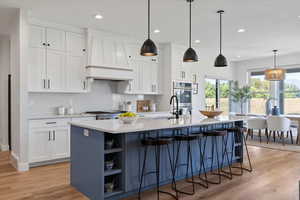 Kitchen featuring white cabinetry, open shelves, hanging light fixtures, light wood-style flooring, and a kitchen breakfast bar