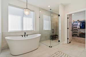 Full bathroom featuring a walk in closet, a soaking tub, a shower stall, light tile patterned floors, and tile walls