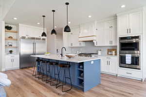 Kitchen featuring open shelves, appliances with stainless steel finishes, white cabinets, a kitchen bar, and an island with sink