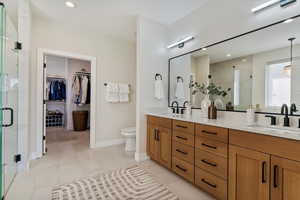 Full bath featuring double vanity, a shower stall, a spacious closet, recessed lighting, and light tile patterned floors