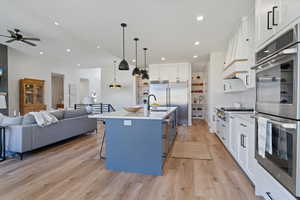 Kitchen with appliances with stainless steel finishes, white cabinets, pendant lighting, a kitchen island with sink, and a kitchen bar