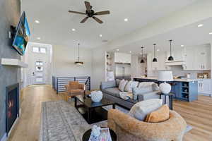Living room with light wood-style flooring, recessed lighting, a warm lit fireplace, and a ceiling fan