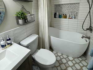 Full bath with a textured ceiling, tile walls, vanity, and a combined bath / shower with freestanding tub