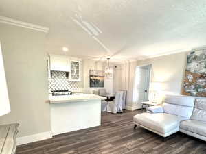 Living room with crown molding, dark wood-style floors, a textured ceiling, and a chandelier