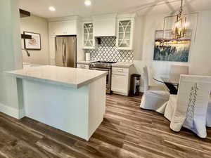 Kitchen featuring glass insert cabinets, white cabinets, backsplash, stainless steel appliances, and pendant lighting