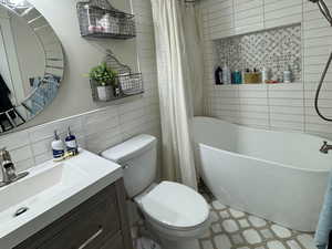 Full bathroom featuring vanity, a textured ceiling, tile walls, and a combined bath / shower with freestanding tub