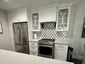 Kitchen featuring glass insert cabinets, white cabinets, stainless steel appliances, and light stone counters