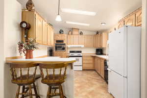 Kitchen featuring white appliances, a kitchen bar, light countertops, a peninsula, and light brown cabinets