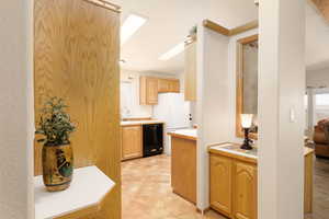 Kitchen with light countertops, black dishwasher, light brown cabinetry, and a skylight