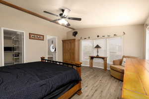 Bedroom with light wood finished floors, vaulted ceiling, a walk in closet, a ceiling fan, and connected bathroom