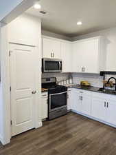 Kitchen featuring stainless steel appliances, dark countertops, white cabinets, tasteful backsplash, and recessed lighting