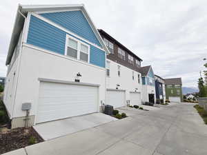 Back of house featuring concrete driveway, a residential view, an attached garage, and stucco siding