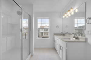 Bathroom featuring double vanity, healthy amount of natural light, light tile patterned floors, and a stall shower