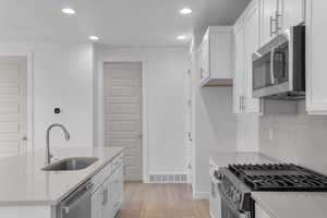 Kitchen featuring stainless steel appliances, light stone countertops, white cabinets, and recessed lighting