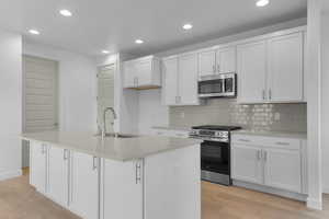 Kitchen with stainless steel appliances, light stone countertops, recessed lighting, light wood-type flooring, and white cabinets