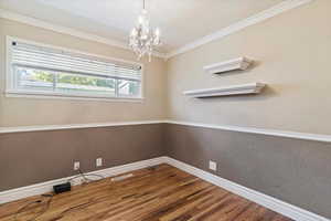 Spare room with crown molding, wood finished floors, a chandelier, and a textured wall