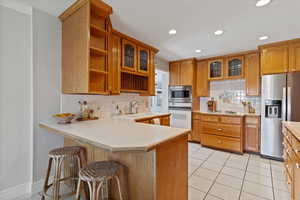 Kitchen with glass insert cabinets, a kitchen bar, light countertops, and recessed lighting