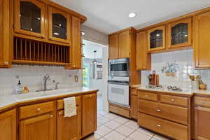 Kitchen featuring glass insert cabinets, light countertops, tasteful backsplash, and brown cabinetry