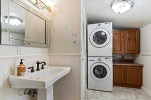 Laundry room with a wainscoted wall, estacked washer and dryer, and cabinet space