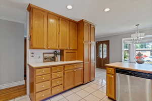 Kitchen with crown molding, light countertops, stainless steel dishwasher, light tile patterned flooring, and hanging light fixtures