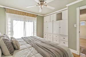Bedroom featuring light wood-type flooring, ornamental molding, and a ceiling fan