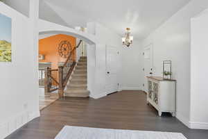 Foyer featuring dark wood-style flooring, stairway, arched walkways, and a chandelier