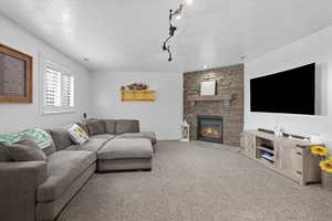 Family room with carpet, a stone fireplace, track lighting, and a textured ceiling