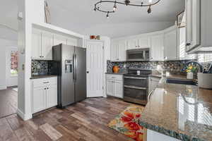 Kitchen featuring healthy amount of natural light, appliances with stainless steel finishes, granite counters, vaulted ceiling, and backsplash