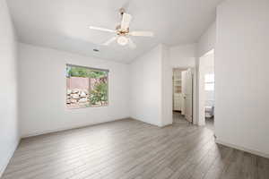 Unfurnished bedroom with a walk in closet, light wood-style floors, a ceiling fan, lofted ceiling, and ensuite bathroom