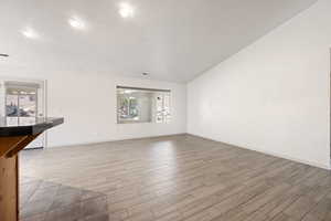 Unfurnished living room featuring light wood-style flooring, lofted ceiling, and recessed lighting