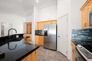 Kitchen with stainless steel appliances, light brown cabinetry, vaulted ceiling, light tile patterned floors, and backsplash